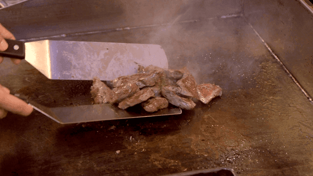 Chef grilling meat on a hot griddle