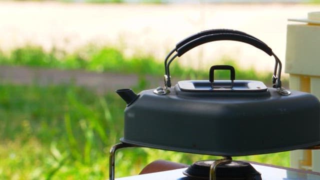 A kettle heating up on a camping stove outdoors