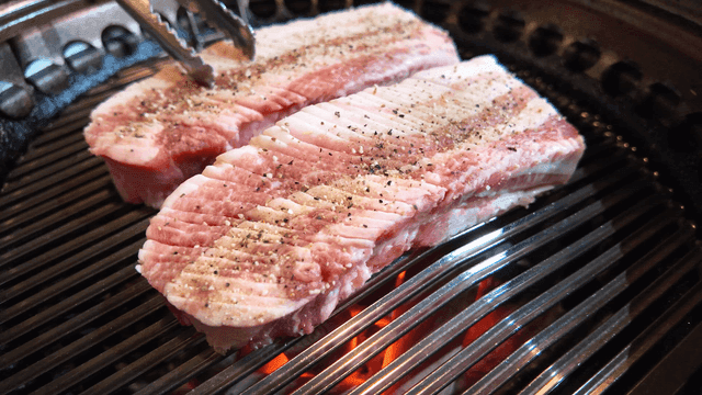 Thick pork belly being grilled on grill