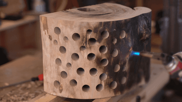 구멍이 많은 나무 조각품을 토치로 그을리는 장인