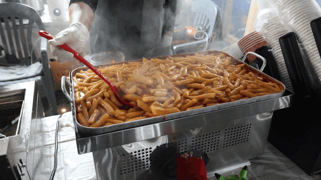 Ladle stirring tteokbokki while cooking in large pan