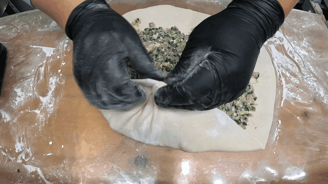 Glove-clad hands rolling up dumpling wrappers