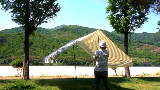 Person setting up a tarp in a scenic outdoor area with mountains in the background