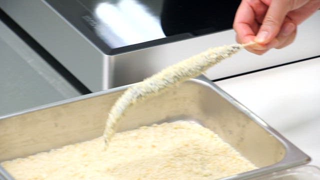 Sand eels with skewers being coated and fried in a pan