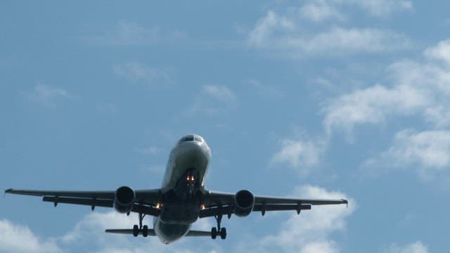 Airplane flying under blue sky with clouds