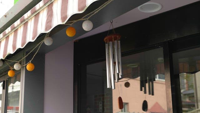 Wind chime hanging under the striped awning outside a storefront during the day