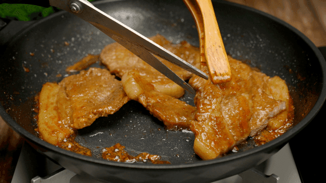 Grilled pork being cut in a pan