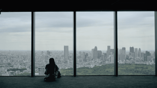 Person sitting by a large window overlooking a cityscape