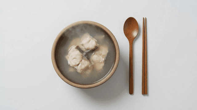 Steaming bowl of clear fish soup along with spoon.