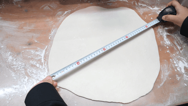Hand measuring length of dough with measuring tape