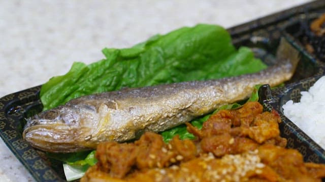 Grilled corvina with a side of spicy stir-fried pork and rice served on a plastic tray