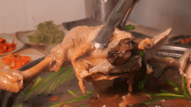 Tongs lifting chicken leg from boiling Samgyetang pot