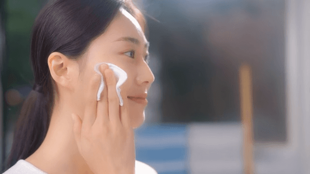 Woman cleansing face with a cotton pad in sunlight