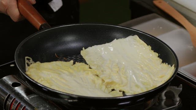 Cabbage pancakes cooked in a hot oiled pan with a wooden spatula