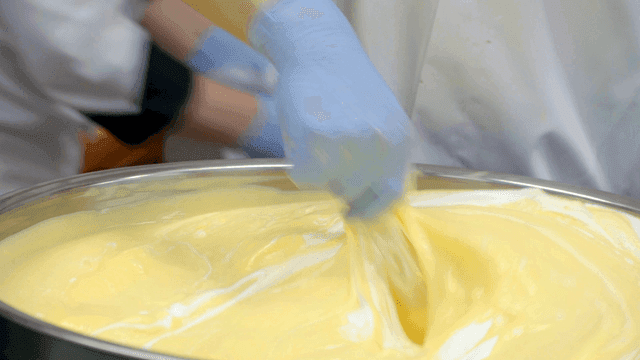 Baker mixing dough in large metal bowl