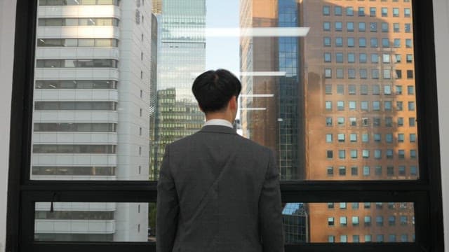 사무실 창밖 높은 건물을 바라보며 스트레칭을 하고 있는 슈트입은 남자