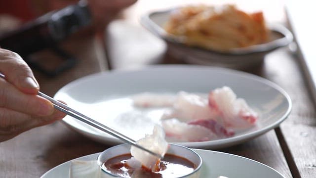 Person dipping raw fish in red chili-pepper paste with vinegar with chopsticks