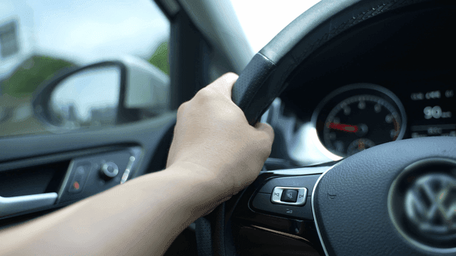 Hands gripping steering wheel while driving car on clear day