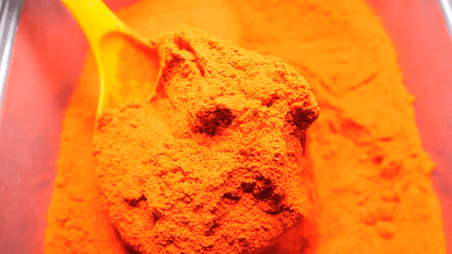 Ladle scooping out bright red chili powder from container