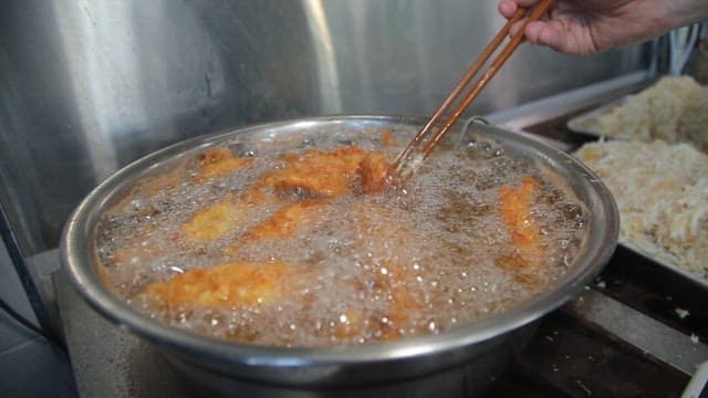 Golden-brown fried food cooking in hot oil being lifted with chopsticks