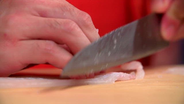 Slicing trimmed flatfish on a wooden cutting board