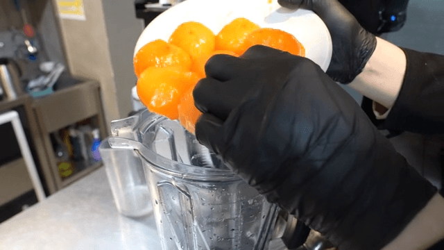 Gloven's hand putting peeled persimmon into blender