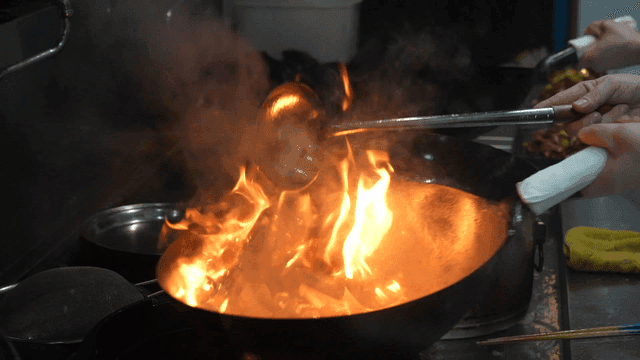 Chef cooking in wok over flame in kitchen