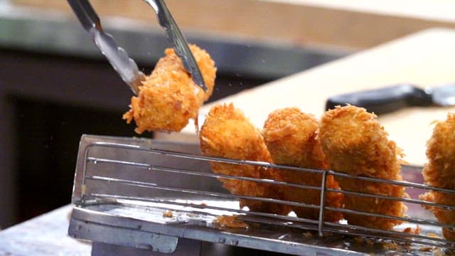 Crispy pork cutlet fried in deep fryer being lifted with tongs