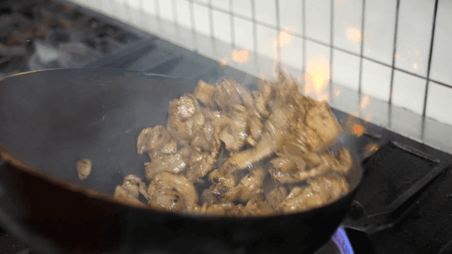 Meat being stir-fried in a pan with flames