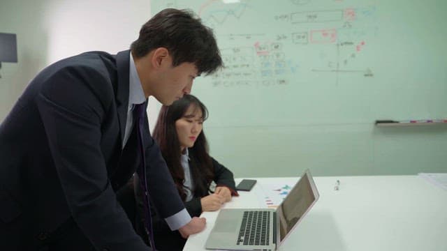 Two people discussing while looking at laptop in office