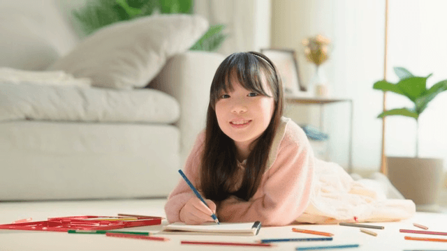 Child lying down in the living room drawing with colored pencils