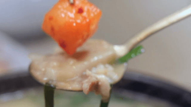 A spoonful of pork and rice soup with diced radish kimchi