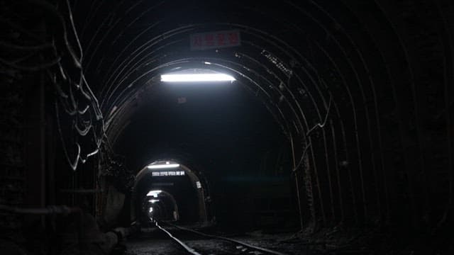 Inside a dark coal mine tunnel, illuminated by dim lights