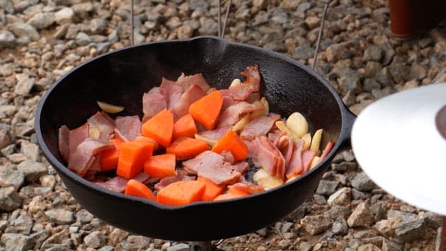 Stir-frying various vegetables and bacon in a heated frying pan