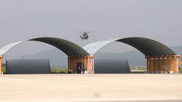 Helicopter hovering above two semi-circle hangars on a cloudy day