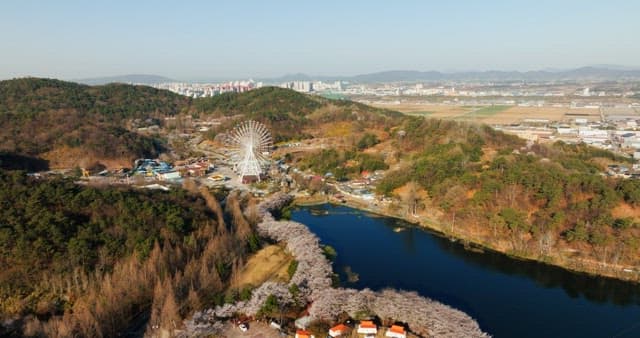 푸르른 숲과 언덕으로 둘러싸인 호수 옆에 있는 관람차가 있는 공원의 전망
