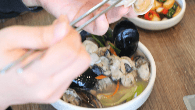 Person who eats oyster kalguksu with mussels and clams using chopsticks
