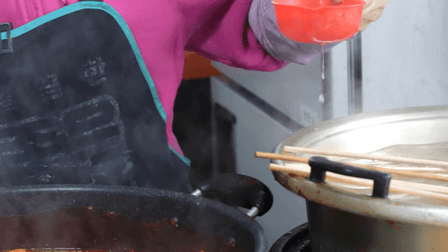 Elderly woman pouring fish cake broth into tteokbokki with ladle