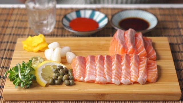 Eating rakkyo and capers on a wooden cutting board with salmon sashimi plated on it