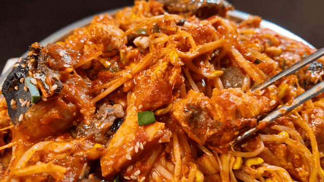 Chopsticks picking up spicy braised anglerfish with seafood and vegetables