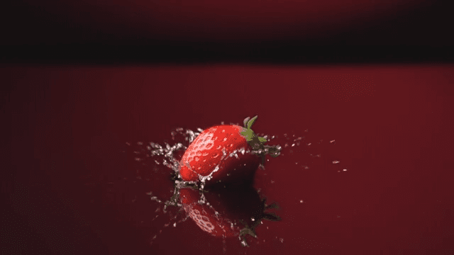 Red strawberries fallen into shallow water on a dark red background