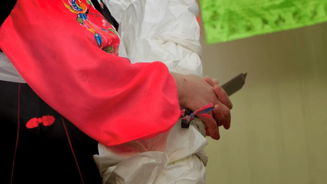 Person in hanbok holding a knife and a bundle of paper