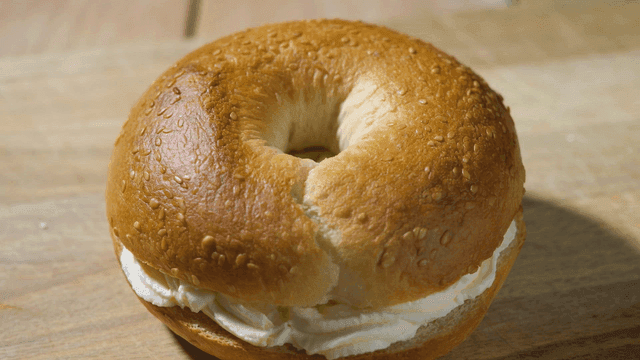 Cream cheese bagel on wooden cutting board.