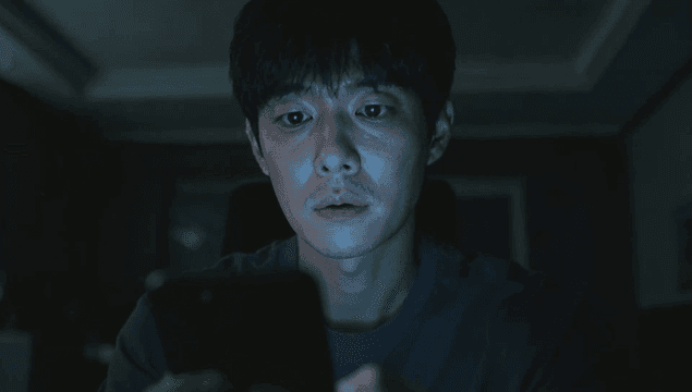 어두운 방에서 휴대폰 화면을 바라보는 남성
