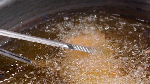 Frying pork in hot oil with tongs