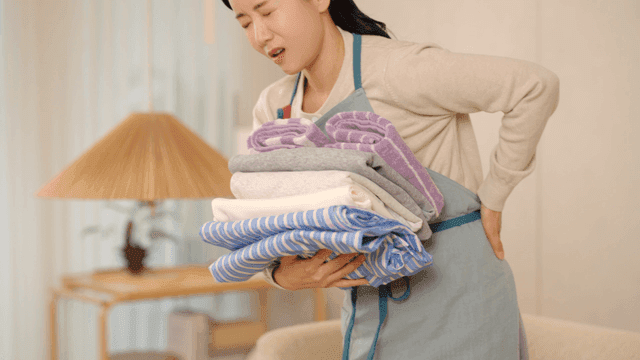 Woman feels back pain while lifting laundry from sofa