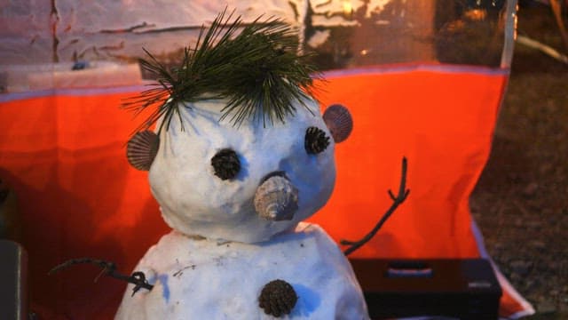 Snowman made with pin cones and seashells next to an orange tent