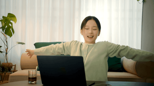 Woman stretching while working on her laptop at home