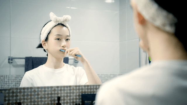 Woman brushing teeth in a bathroom mirror