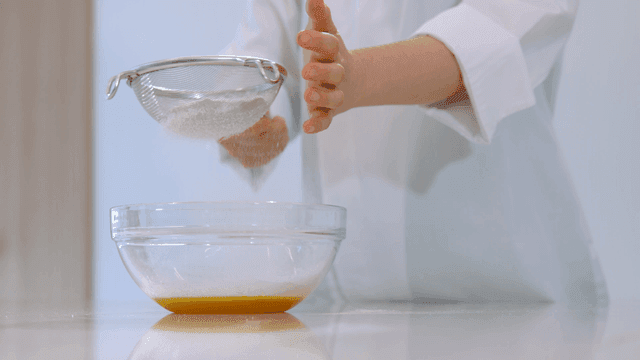 Baker sifting flour over egg mixture